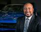 A person wearing a suit and tie in front of a car
Description generated with very high confidence
